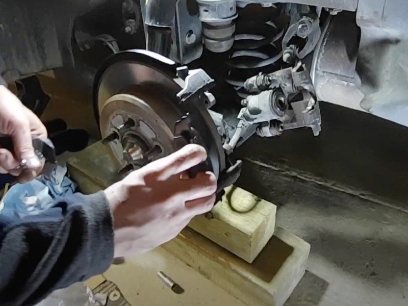 Mobile auto repair mechanic installing new brake pads in the caliper of a disc brake job.