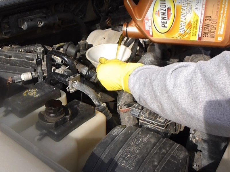 Motor oil being added to a vehicle engine after an oil change by a mobile auto repair technician.